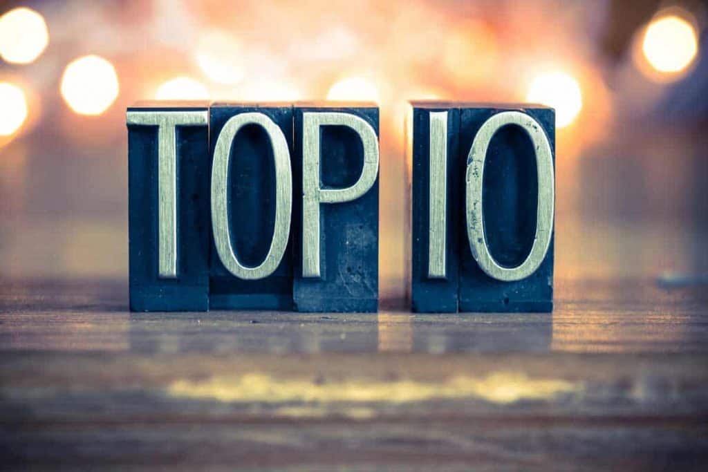 Metall-Buchdruckblöcke bilden auf einer Holzfläche die Aufschrift „TOP 10“, vor einem verschwommenen Hintergrund aus warmem Licht.