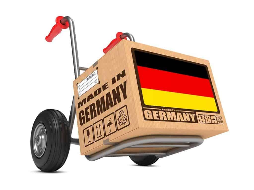 Auf einer Sackkarre steht ein Karton mit der Aufschrift „Made in Germany“ und einer deutschen Flagge. Auf dem Karton sind außerdem Handhabungssymbole und Versandetiketten zu sehen.
