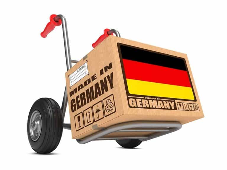 Auf einer Sackkarre steht ein Karton mit der Aufschrift „Made in Germany“ und einer deutschen Flagge. Auf dem Karton sind außerdem Handhabungssymbole und Versandetiketten zu sehen.