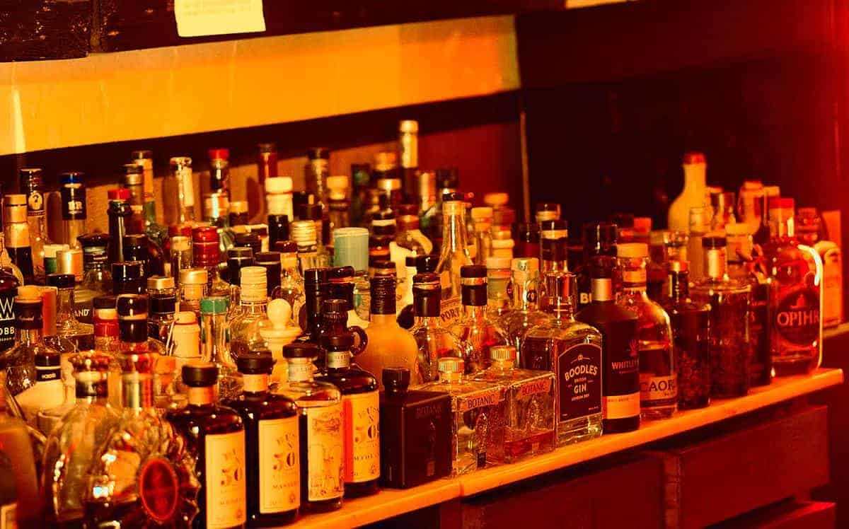 Ein Barregal, gefüllt mit verschiedenen Flaschen mit Spirituosen und Likören, darunter Whisky, Gin und Rum, die in Reihen unter warmem gelb-orangefarbenem Licht angeordnet sind.