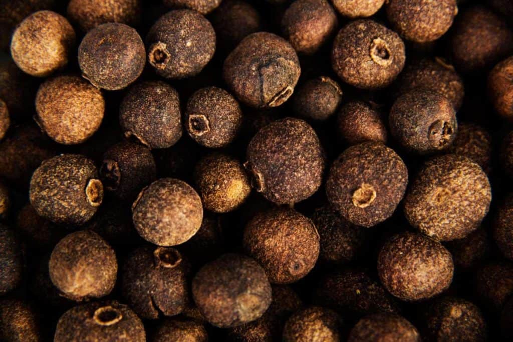 Eine Nahaufnahme von ganzen Pimentbeeren, die ihre raue, braune Oberfläche und ihre runde Form zeigen, dicht aneinander gereiht.