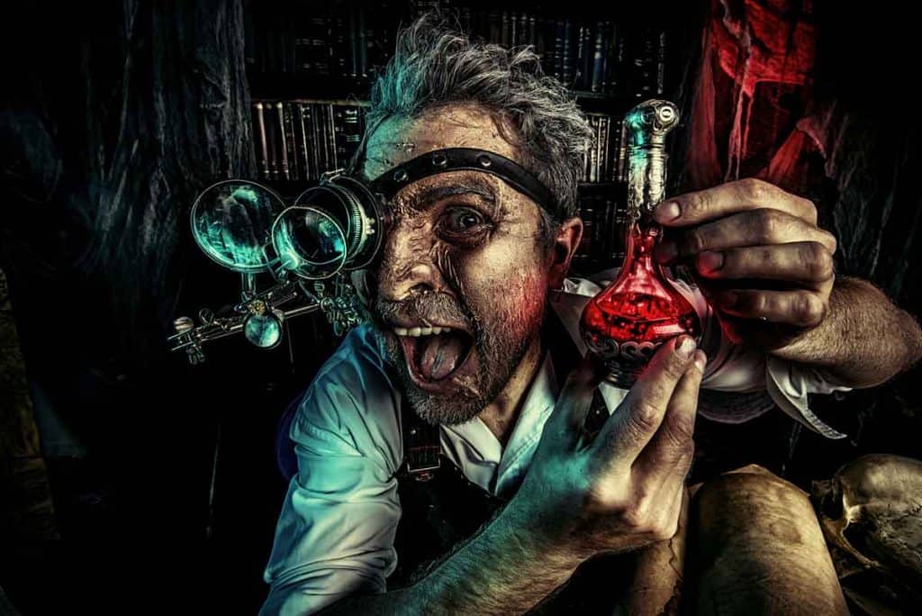 Ein Wissenschaftler mit wildem Blick und zerzaustem Haar hält einen roten Zaubertrank in einem Kolben in der Hand, trägt eine Steampunk-Schutzbrille und schneidet in einem dunklen, überfüllten Labor eine alberne Grimasse, während er die Zunge herausstreckt.