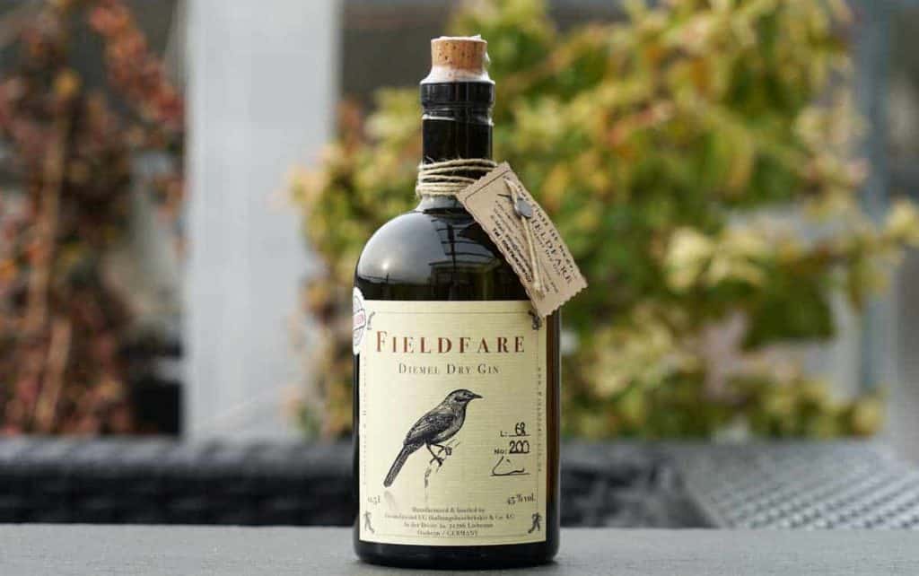 Eine Flasche „Fieldfare Derne Dry Gin“ mit Korkverschluss und einem Etikett, auf dem ein Vogel abgebildet ist, im Freien ausgestellt vor einem Hintergrund aus verschwommenem Grün.
