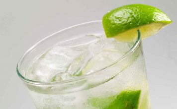 Gin Rickey – Gin Cocktail Eine Nahaufnahme eines kalten Glases, gefüllt mit Eis, einem klaren, sprudelnden Getränk und Limettenscheiben, wobei der Rand mit einer Limettenscheibe verziert ist.