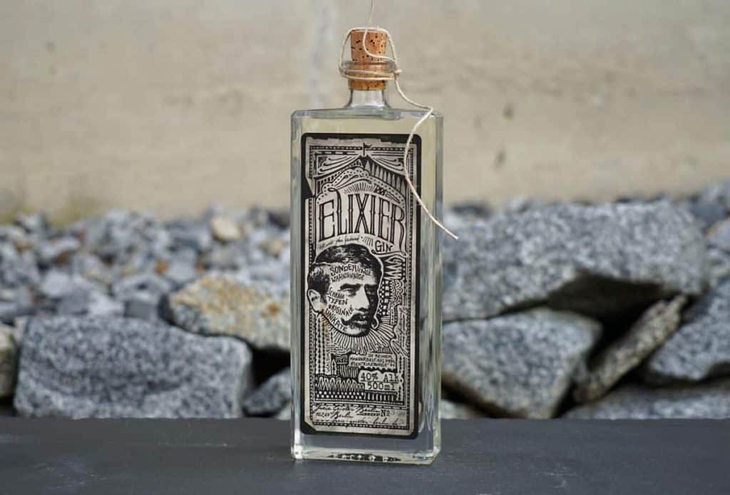 Auf einer dunklen Fläche steht eine durchsichtige Glasflasche mit der Aufschrift „Elixier“ und einem Korkverschluss. Auf dem Etikett ist eine Illustration im Vintage-Stil zu sehen, die den Kopf eines Mannes darstellt. Im Hintergrund sind graue Felsen zu sehen.