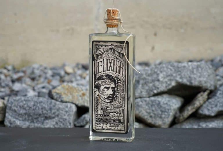Auf einer dunklen Fläche steht eine durchsichtige Glasflasche mit der Aufschrift „Elixier“ und einem Korkverschluss. Auf dem Etikett ist eine Illustration im Vintage-Stil zu sehen, die den Kopf eines Mannes darstellt. Im Hintergrund sind graue Felsen zu sehen.