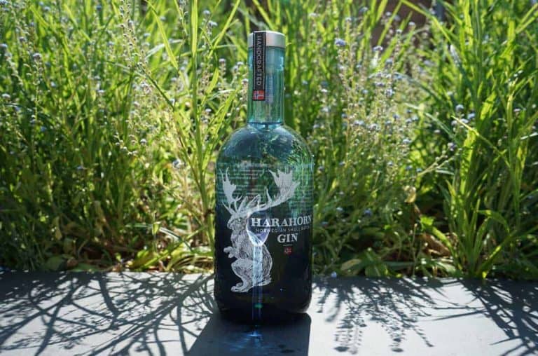 Eine Flasche Harahorn-Gin steht im Freien auf einer schwarzen Fläche, umgeben von hohem grünem Gras und Wildblumen im strahlenden Sonnenlicht.