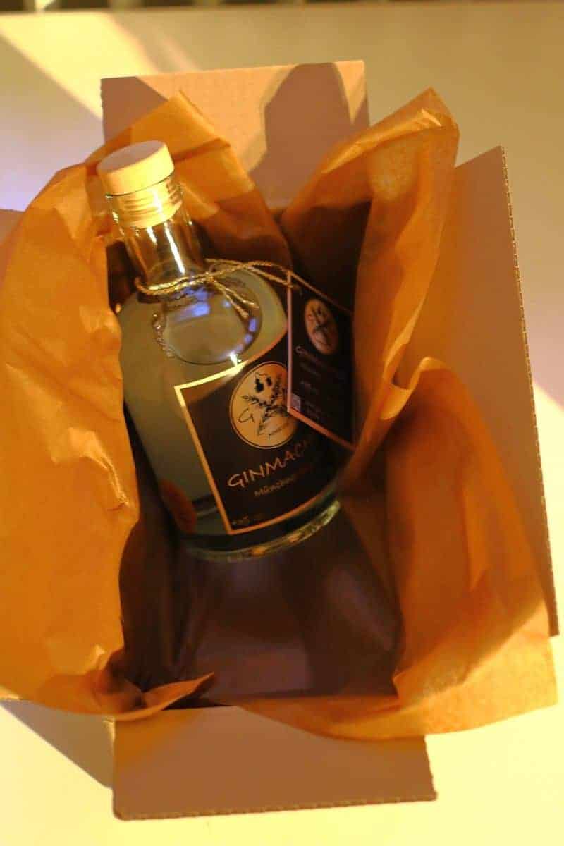 Eine Flasche GinMare-Gin steht in einem mit orangefarbenem Seidenpapier ausgekleideten Karton, bereit zum Verschenken oder Versenden.