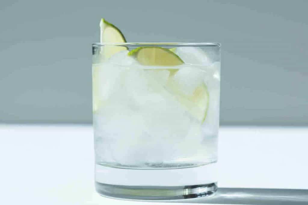 Ein mit Eiswürfeln gefülltes, klares Glas, garniert mit zwei Limettenschnitzen, vor einem schlichten, hellen Hintergrund.