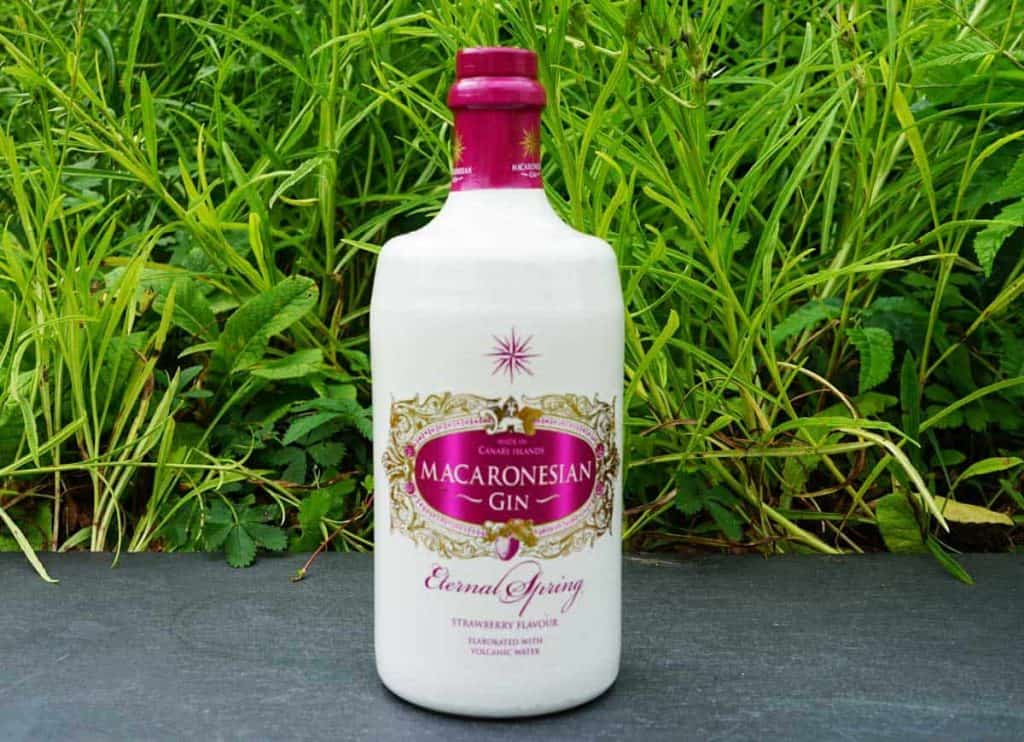 Eine weiße Flasche „Macaronesian Gin“ mit einem rosa Verschluss und einem Etikett mit der Aufschrift „Eternal Spring“ steht auf einer dunklen Fläche, im Hintergrund ist grünes Gras zu sehen.