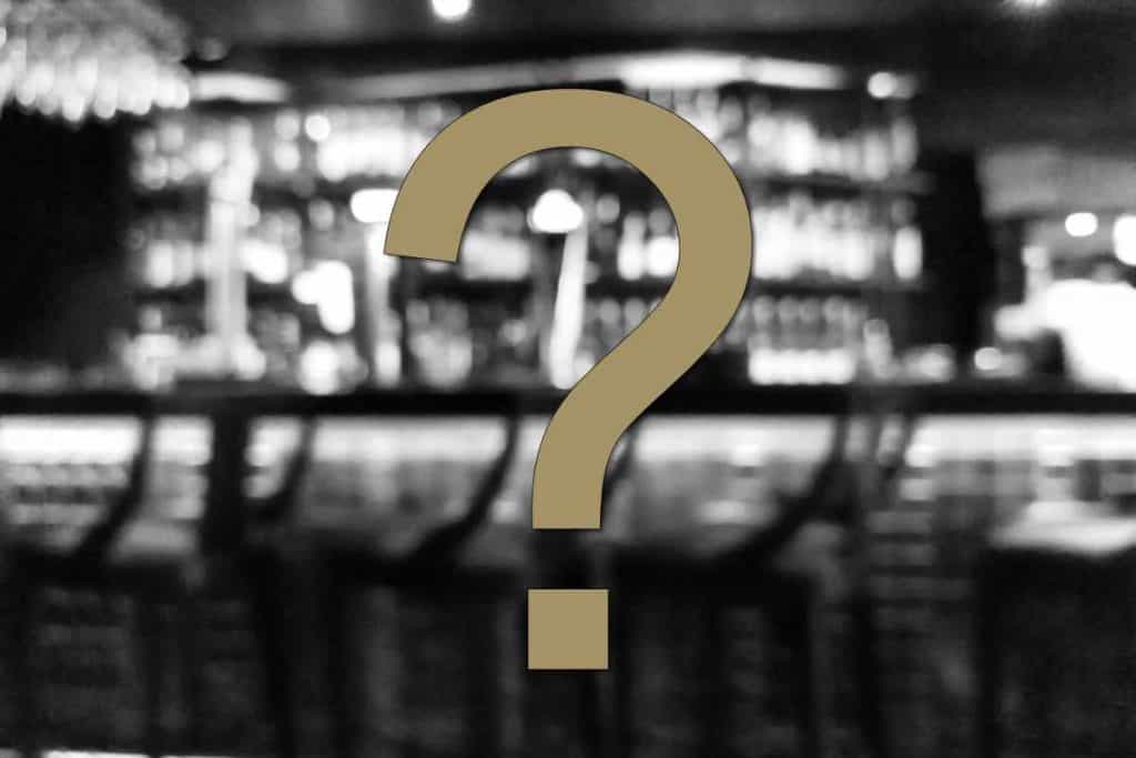 Ein großes Fragezeichen überlagert ein verschwommenes Bild einer leeren Bar mit Barhockern und Regalen voller Flaschen im Hintergrund und regt den Betrachter auf subtile Weise zum Nachdenken an: Wie lagert man Gin richtig?.
