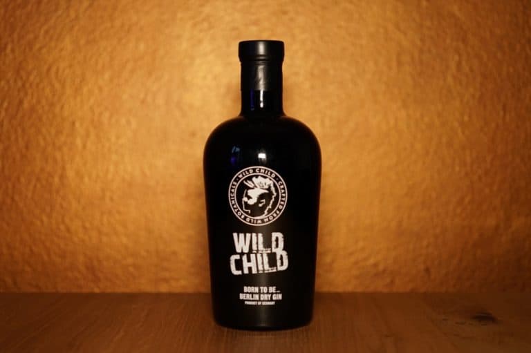 Eine schwarze Flasche mit der Aufschrift „Wild Child Gin“ steht auf einer Holzunterlage vor einem strukturierten goldbraunen Hintergrund und verkörpert die kühne Eleganz des Wild Child Berlin Dry Gin.