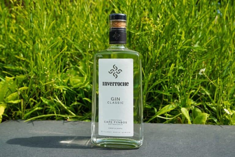 Eine Flasche Inverroche Gin Classic steht im Freien auf einer dunklen Fläche, im Hintergrund sind hellgrünes Gras und Laub zu sehen.