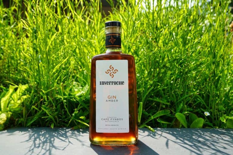Eine Flasche Inverroche Gin Amber steht im Freien auf einer grauen Fläche, wobei ihre elegante Form einen wunderschönen Kontrast zum hohen grünen Gras im Hintergrund bildet.