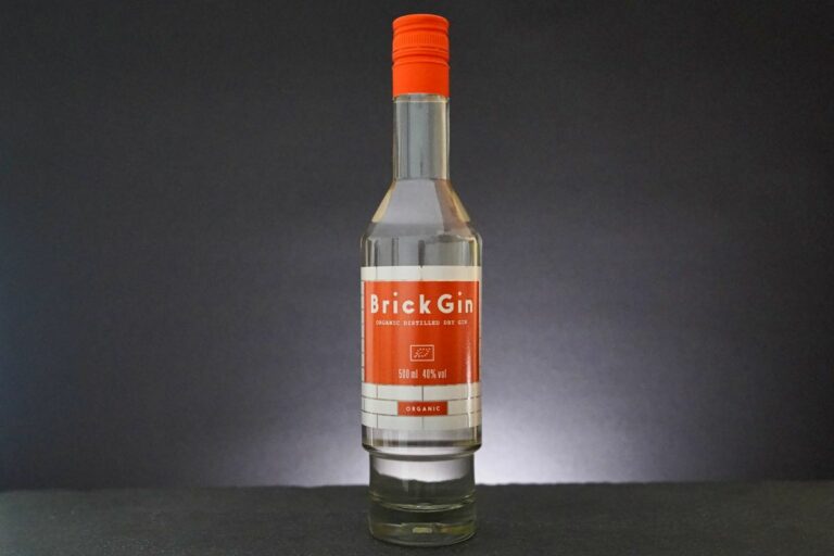 Eine klare Glasflasche „Brick Gin“ mit orangefarbenem Verschluss und Etikett ist vor einem dunklen Hintergrund zu sehen. Auf dem Etikett sind deutlich die Aufschriften „Brick Gin“, „Organic Distilled Dry Gin“ sowie „500 ml, 40,5 % vol.“ zu erkennen, die das unverwechselbare Erscheinungsbild dieses außergewöhnlichen Gins unterstreichen.