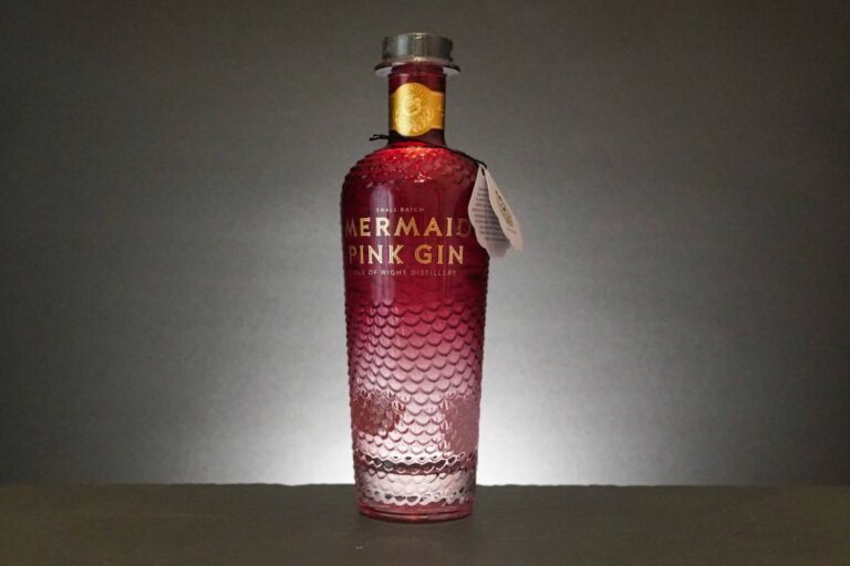 Eine Flasche „Mermaid Pink Gin“ mit einem strukturierten, schuppenartigen Muster und einem Farbverlauf, der vom transparenten Unterteil zum rosa Oberteil übergeht, hebt sich elegant vom grauen Hintergrund ab und unterstreicht das auffällige Design des „Mermaid Pink Gin“.