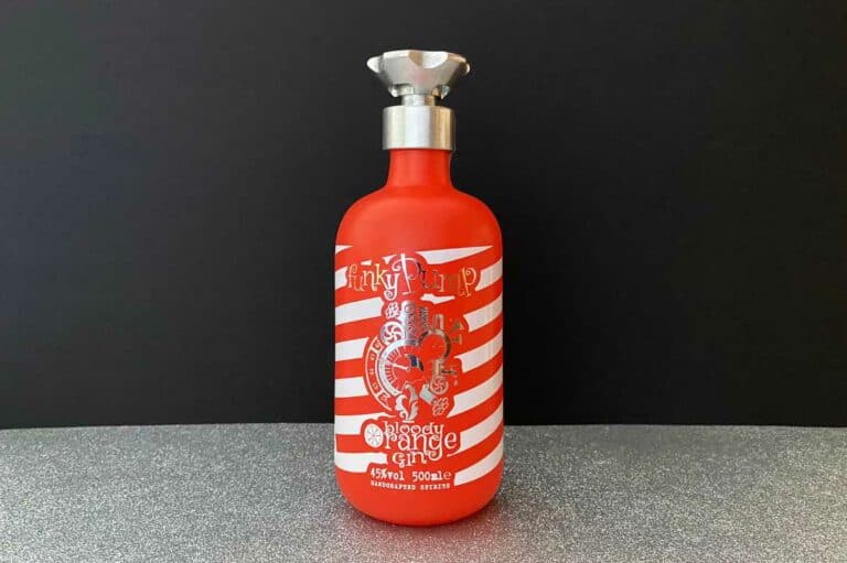 Auf einer glitzernden silbernen Fläche vor schwarzem Hintergrund steht eine rot-weiß gestreifte Flasche mit der Aufschrift „Funky Pump Orange Gin“.