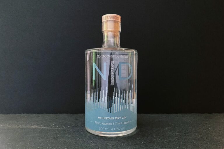 Eine durchsichtige Flasche „Mountain Gin“ der Northbottens Distillery steht vor einem schwarzen Hintergrund; ihr blau-weißes Etikett erinnert an frische Alpenluft. Mit Zutaten wie Birke, Angelika und Timur-Pfeffer fängt dieser „Mountain Dry Gin“ bei jedem Glas die Essenz des Hochlands ein.