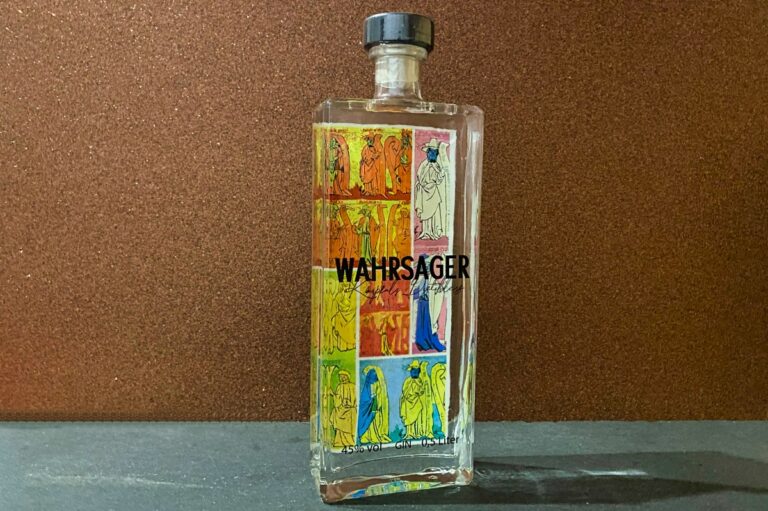Eine durchsichtige Flasche mit der Aufschrift „Wahrsager Gin“, verziert mit farbenfrohen, illustrierten Motiven von Figuren in roten, gelben, blauen und weißen Gewändern auf braunem Hintergrund.