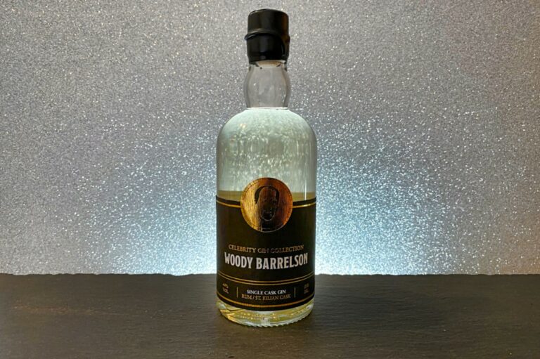 Auf einer dunklen Fläche vor einem funkelnden silbernen Hintergrund steht eine Flasche mit der Aufschrift „Woody Barrelson Single Cask Gin“ aus der Celebrity Gin Collection.
