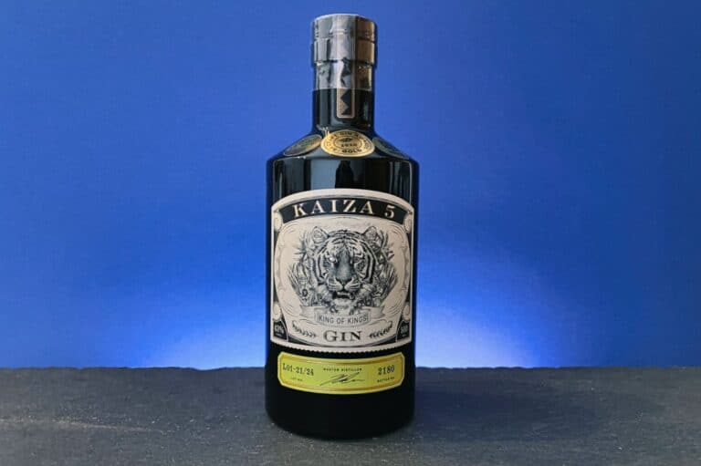 Eine schwarze Flasche „Kaiza 5 Gin“ mit einer detailreichen Tigerillustration auf dem Etikett ist vor einem blauen Hintergrund auf einer dunklen Unterlage platziert.