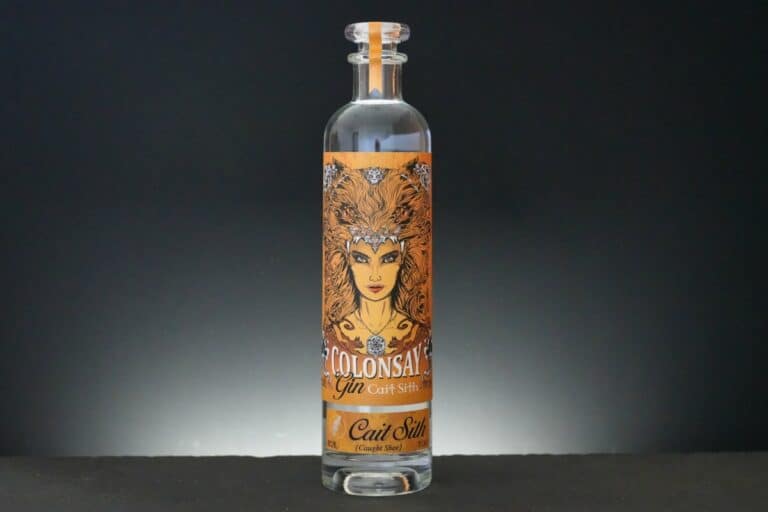 Eine hohe, durchsichtige Glasflasche mit Colonsay Gin, auf deren Etikett eine Frau mit feurigem Haar abgebildet ist, zusammen mit dem Schriftzug „Colonsay Gin Cait Sith“ und darunter „Cait Sith“.