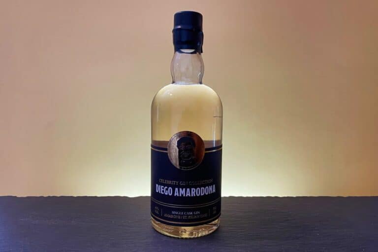 Eine Flasche der „Celebrity Gin Collection“ mit der Aufschrift „Diego Amarodona Single Cask Gin“ steht auf einer dunklen Fläche vor einem beigefarbenen Hintergrund mit Farbverlauf und wird von hinten sanft beleuchtet.