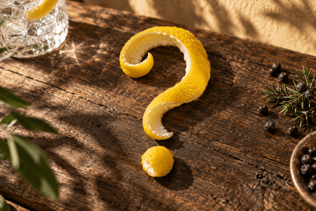 Fragezeichen aus Zitronenzeste neben einem Gin-Drink auf einem Holztisch