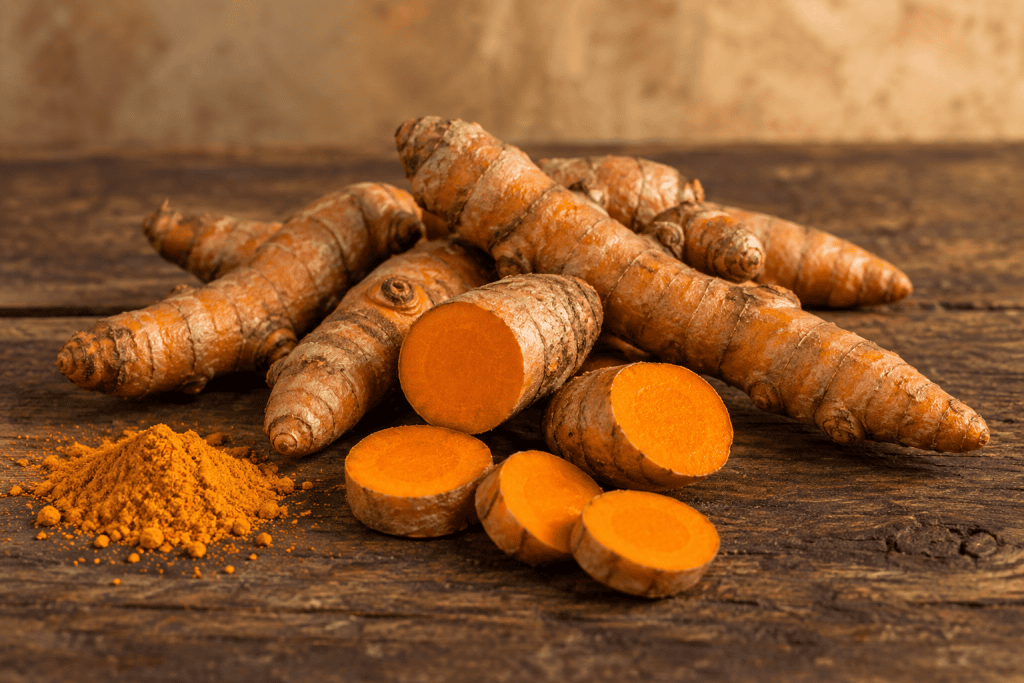 Kurkumawurzeln, aufgeschnitten mit orangem Inneren, und Kurkumapulver